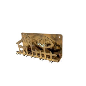 May include: A brass key holder featuring a house, tree, and picket fence design. The key holder has seven hooks and is mounted on a rectangular plate. The metal has a warm, golden hue.