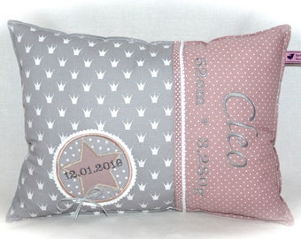 Op de afbeelding: Een grijs en roze kussen met een wit kroonpatroon en de tekst "Cleo 52 cm * 3.280 g 12.01.2019" erop geborduurd.