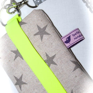 Puede incluir: Una peque&ntilde;a bolsa de tela beige con una correa amarilla brillante y un patr&oacute;n de estrellas grises. La bolsa tiene una etiqueta que dice "Spatz Handm".