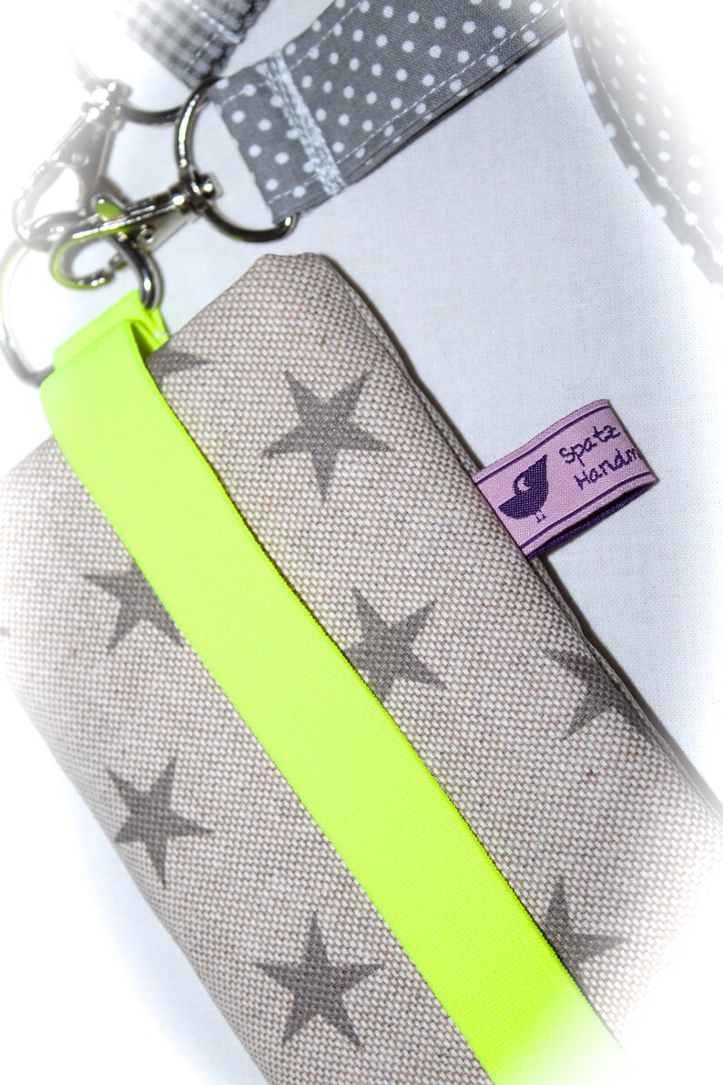 Puede incluir: Una peque&ntilde;a bolsa de tela beige con una correa amarilla brillante y un patr&oacute;n de estrellas grises. La bolsa tiene una etiqueta que dice "Spatz Handm".