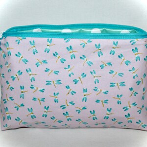 May include: A light purple zippered pouch with a teal zipper and a teal and white polka dot lining. The pouch is covered in a pattern of teal dragonflies. The pouch has a teal tag with the text "You Are My Sunshine" in white.