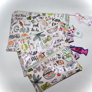 Könnte beinhalten: Drei rosa und weiße Reißverschlusstaschen mit verschiedenen bunten Illustrationen und Texten, darunter "Add More Spice", "Good", "Keep Nut", "GRR!" und "FUN".