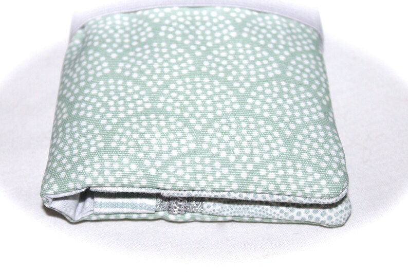 May include: A green zippered pouch with a white polka dot pattern. The pouch is folded and the zipper is visible.
