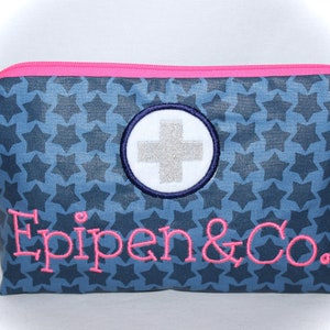 Könnte beinhalten: Eine blaue Reißverschlusstasche mit einem weißen Sternenmuster. Die Tasche hat einen rosa Reißverschluss und ein weiß gesticktes Kreuz in einem blauen Kreis. Der Text "Epipen & Co." ist in rosa auf der Vorderseite der Tasche gestickt.