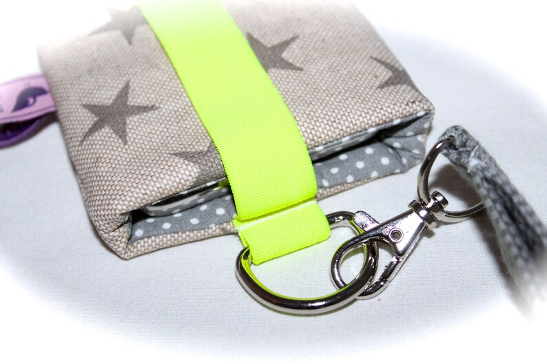 Puede incluir: Una peque&ntilde;a bolsa de tela beige con una correa amarilla ne&oacute;n y un cierre de metal plateado. La bolsa tiene un forro de lunares blancos y grises y un patr&oacute;n de estrellas grises y blancas en el exterior.