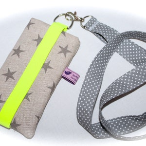 Puede incluir: Una funda para tel&eacute;fono de tela gris con una correa amarilla fluorescente y un patr&oacute;n de estrellas blancas. La funda tiene un clip giratorio plateado y un cord&oacute;n gris y blanco con lunares.