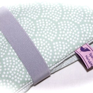 May include: A green fabric pouch with white polka dots and a gray ribbon closure. The pouch has a pink label with purple text that reads "spotz handmade".