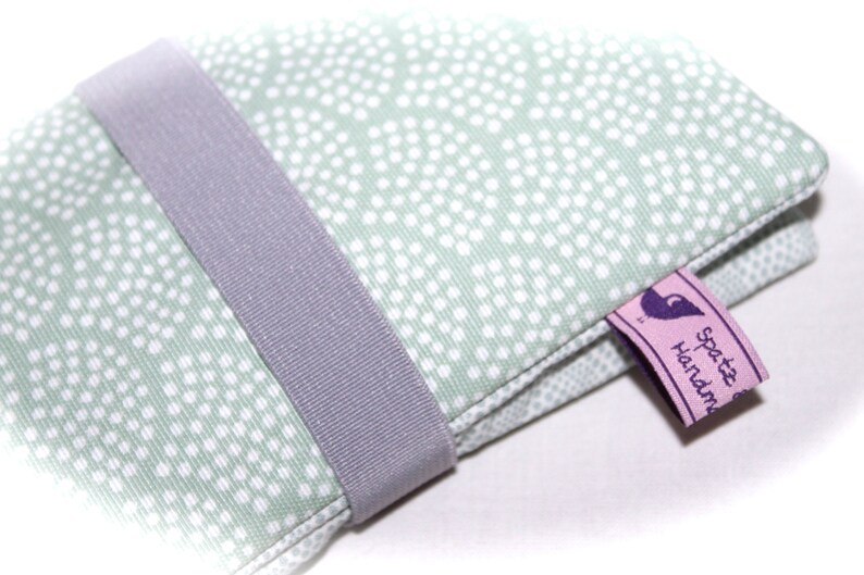 May include: A green fabric pouch with white polka dots and a gray ribbon closure. The pouch has a pink label with purple text that reads "spotz handmade".
