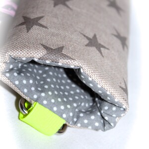 Puede incluir: Una peque&ntilde;a bolsa con un exterior de tela beige con un patr&oacute;n de estrellas repetido. La bolsa est&aacute; forrada con una tela gris con lunares blancos. Una correa amarilla brillante con herrajes plateados est&aacute; unida a la bolsa.