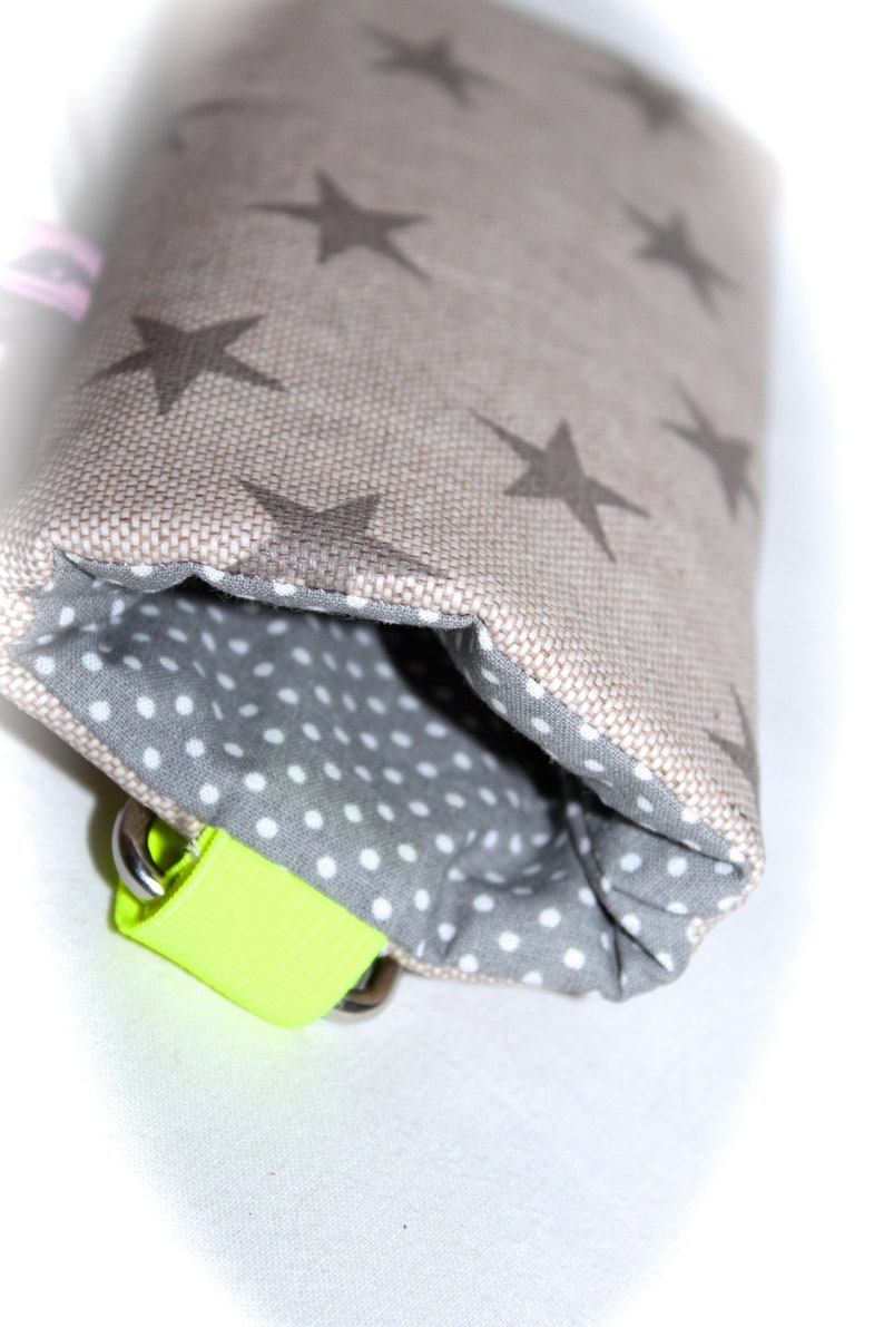 Puede incluir: Una peque&ntilde;a bolsa con un exterior de tela beige con un patr&oacute;n de estrellas repetido. La bolsa est&aacute; forrada con una tela gris con lunares blancos. Una correa amarilla brillante con herrajes plateados est&aacute; unida a la bolsa.