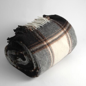 May include: A rolled up plaid throw blanket with brown, white and grey stripes. The blanket has a fringe edge.