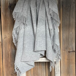 May include: A grey wool throw blanket with fringe on the edges, draped over a wooden ladder.