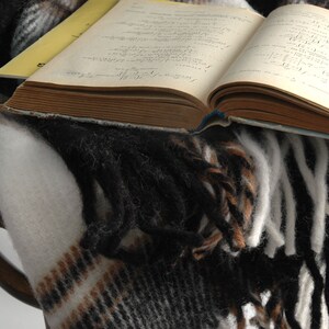 May include: A vintage book with handwritten notes lies open on a brown and white plaid blanket with fringe.