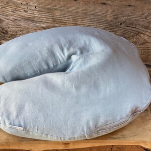 May include: A light blue linen pregnancy pillow shaped like a horseshoe. The pillow has a zipper on one side.