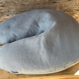 May include: A light blue, U-shaped pillow made of linen fabric. The pillow is designed for comfort and support.
