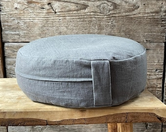 May include: A gray round meditation cushion with a seam around the middle. The cushion is made of a soft, textured fabric.