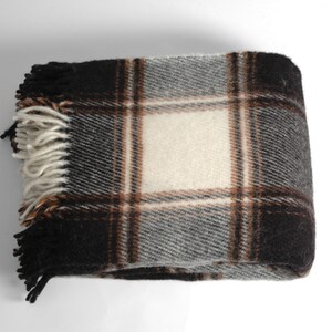 May include: A brown, black and white plaid throw blanket with fringe on the edges.
