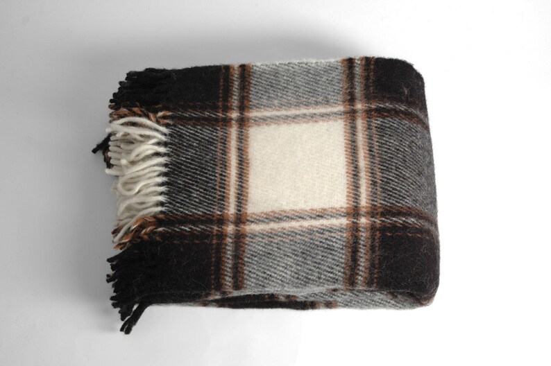 May include: A brown, black and white plaid throw blanket with fringe on the edges.