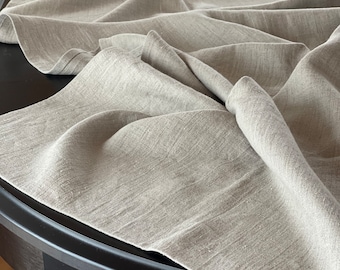 May include: A close-up of a light gray linen tablecloth draped over a black round table. The tablecloth is wrinkled and has a natural, textured look.