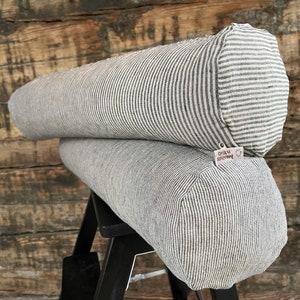May include: Two striped bolster pillows, one on top of the other, with a small tag that says "Oriku Spilven" on the bottom pillow.