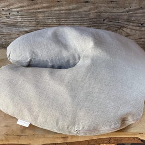 May include: A light gray U-shaped pillow made of linen fabric. The pillow has a zipper closure and is designed for comfort and support.