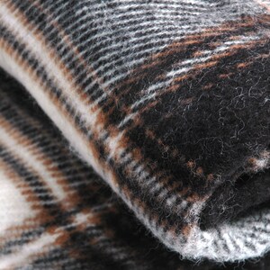 May include: A close-up of a soft, brown, black and white plaid blanket. The blanket is folded in half and the texture of the fabric is visible.