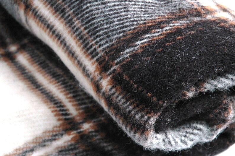 May include: A close-up of a soft, brown, black and white plaid blanket. The blanket is folded in half and the texture of the fabric is visible.