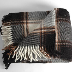 May include: A brown, grey and white plaid throw blanket with fringe on all sides. The blanket is folded in half and the fringe is visible on the bottom and sides.