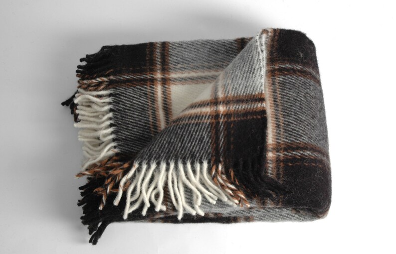 May include: A brown, grey and white plaid throw blanket with fringe on all sides. The blanket is folded in half and the fringe is visible on the bottom and sides.