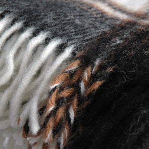 May include: A close-up of a black, brown and white woven blanket with a fringed edge. The blanket is made of soft, fuzzy fibres.