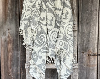 Puede incluir: Una manta blanca con un patrón paisley gris y flecos cuelga de una escalera de madera.