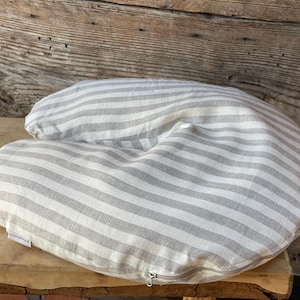May include: A gray and white striped nursing pillow with a curved shape. The pillow has a zipper closure and is made of a soft fabric. The pillow is designed for comfort and support during breastfeeding.
