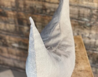 May include: A grey and white striped linen pillow in the shape of a crescent moon. The pillow is sitting on a wooden surface.