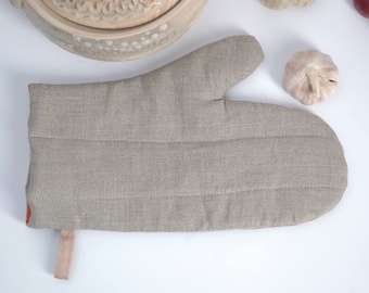 May include: A beige linen oven mitt with red trim and a beige strap. The mitt is quilted and has a textured surface.