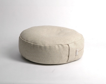 May include: A round, beige meditation cushion with a zipper closure. The cushion is made of a textured fabric.