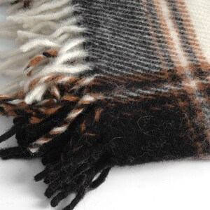 May include: Close-up of a black, brown and white plaid woven fabric with fringe. The fabric has a soft, fuzzy texture.