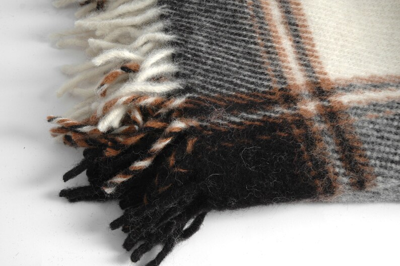 May include: Close-up of a black, brown and white plaid woven fabric with fringe. The fabric has a soft, fuzzy texture.