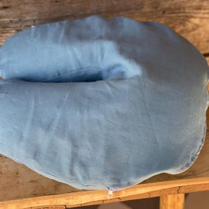 May include: A light blue horseshoe-shaped pillow made of fabric. The pillow is sitting on a wooden surface.