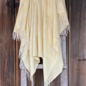May include: A yellow throw blanket with white fringe hanging on a wooden ladder.