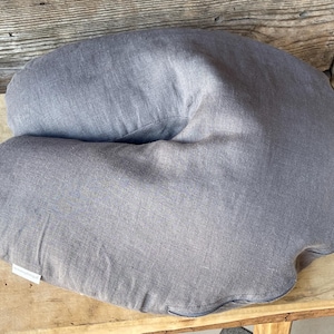 May include: A gray, crescent-shaped pillow made of a soft, textured fabric. The pillow is designed to provide support for the neck and head.