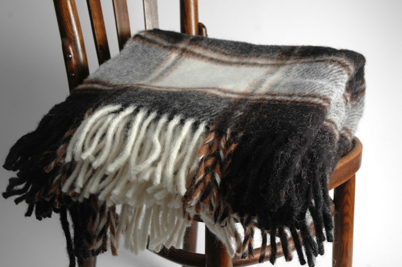 May include: A black, brown and white plaid throw blanket with fringe on a wooden chair.
