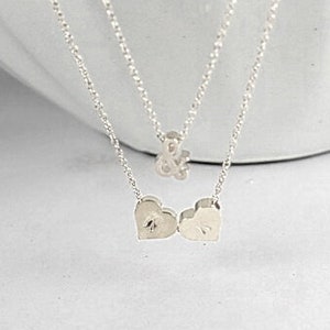 May include: A silver necklace with two heart charms and a smaller charm in the shape of an ampersand.