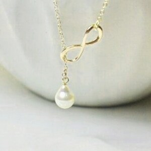 May include: A gold infinity symbol necklace with a single white pearl pendant.