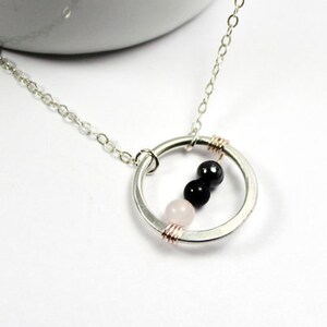May include: A silver necklace with a circle pendant featuring three beads: a pink, a black, and another black bead.