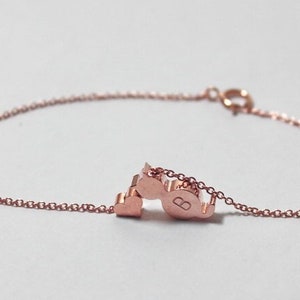 May include: A rose gold chain bracelet with a heart charm and a letter 'B' charm.