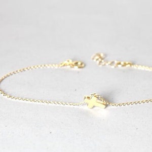 Puede incluir: Un delicado brazalete de cadena dorada con un pequeño dije en forma de cruz.