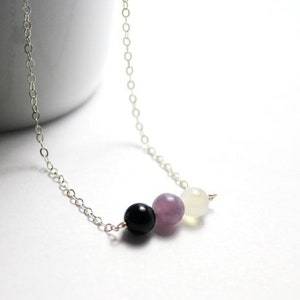 May include: A silver chain necklace with three beads: a black bead, a light purple bead, and a white bead.