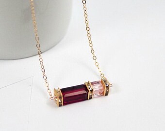 May include: A gold chain necklace with a red and pink crystal pendant. The pendant is made of two rectangular crystals, one red and one pink, set in gold.