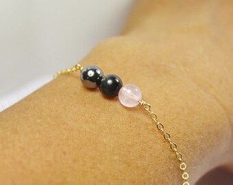 Puede incluir: Un brazalete de cadena dorada con tres cuentas: dos negras y una rosa.