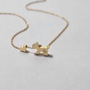 May include: A gold necklace with a small heart charm and a larger dog charm. The dog charm has the letter "S" engraved on it.
